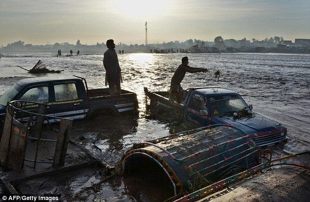 Traders try to prevent their vehicles being washed away by floodwaters near the city of Peshawar