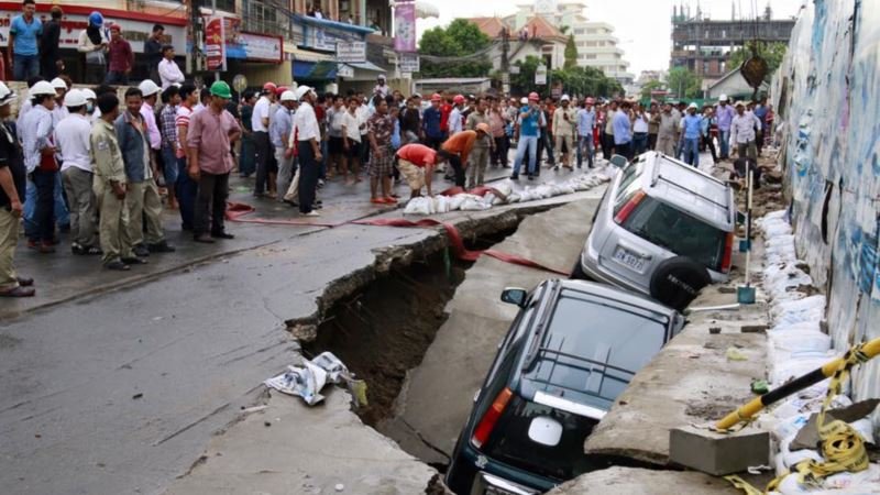 Onlookers watch the cars sink in a hole by a construction site by Phnom Penh's Olympic Stadium after a heavy rain on Wednesday, June 8, 2016. 