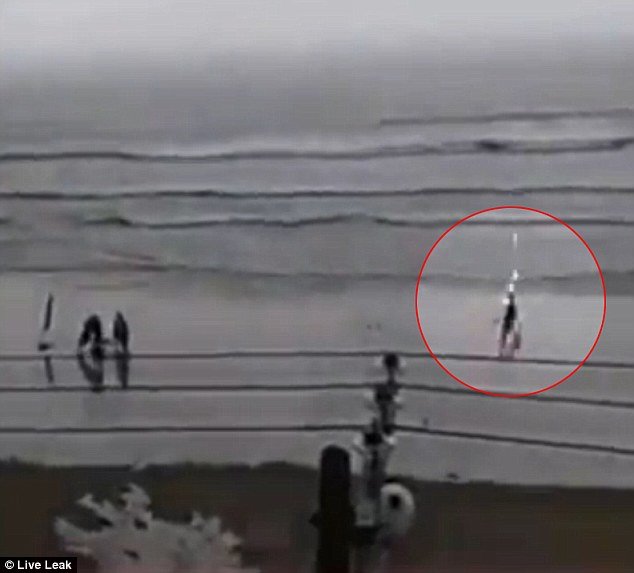 Video shows the woman walking down a rainy beach when lightning strikes
