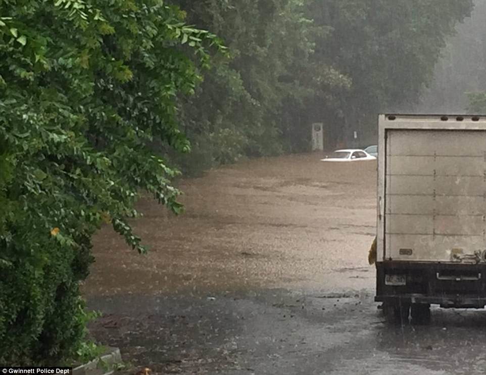 Two dozen people had to be rescued from a flooded parking lot in Georgia, where the water was chest-deep on Tuesday. Pictured, the water reaching up to the car's windows  