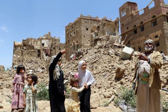 People stand in front of houses destroyed by Saudi-led air strikes in the Yemeni city of Saada () War Saudi Arabia
