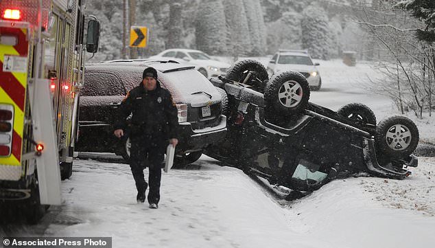 A police officer walks from the scene of an overturned Jeep after an accident on a snow covered road in Richmond, Va., Wednesday, Jan. 17, 2018.