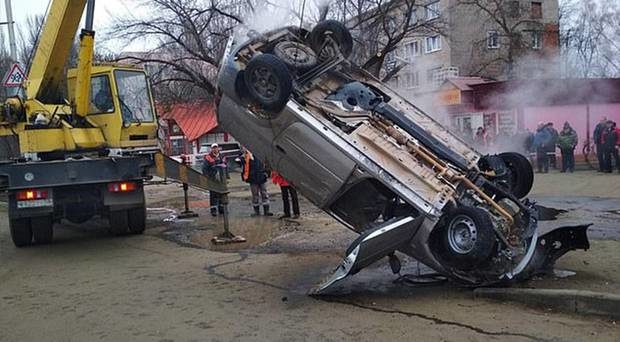 The steaming wreckage of the Lada is seen in the middle of the road today after it plunged into a sink hole full of hot water.