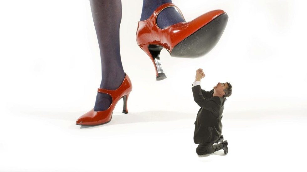 Woman in red high heels stepping on a shrunken man