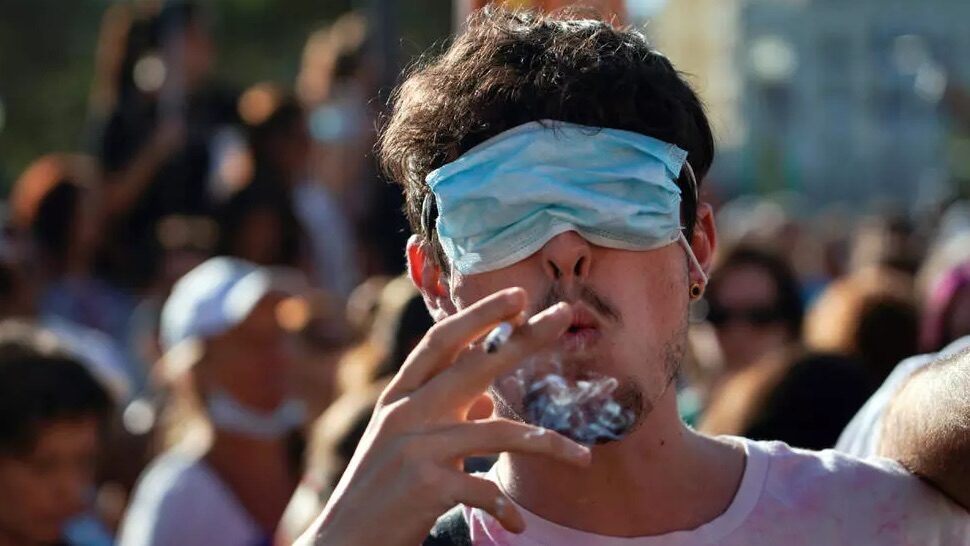 man smokes a cigarette with his eyes covered by a face mask