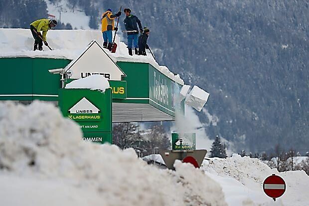 People clear the roof of a petrol station from snow, in Lienz, Austria, Monday, Jan. 4, 2021.