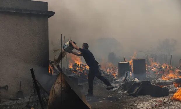 A police officer tries to extinguish the wildfire burning in the village of Vatera, Lesbos.