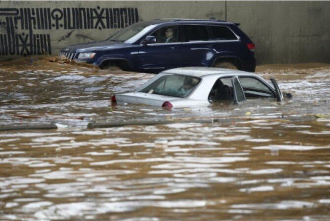 A man, background, drives his car in front a car submerged in flood water at a highway flooded by the rains, in Beirut on Dec. 23, 2023. (