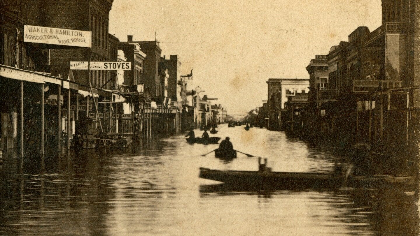 Shows buildings including Baker & Hamilton, Gilday; flooded streets with men in rowboats.