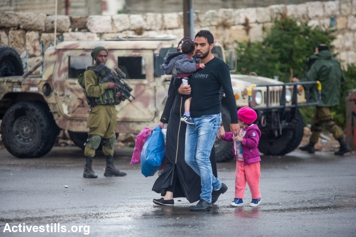 Israeli soldiers stand as palestinian walk