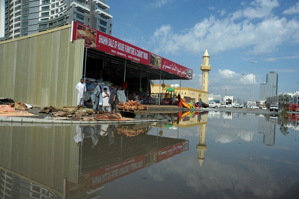 Men look out towards a flooded street in Qirfa. 