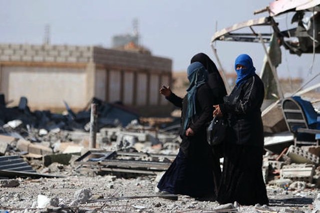 Syrian women walk on rubble