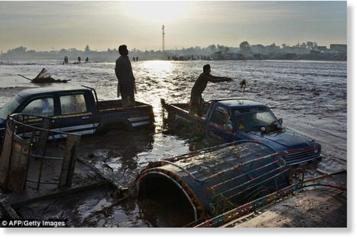 Traders try to prevent their vehicles being washed away by floodwaters near the city of Peshawar