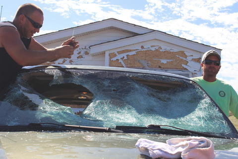 Charles Gall, left, and TJ Hines, attempt to break out the rest of a windshield that was broken during a Sunday evening storm in Killdeer. 