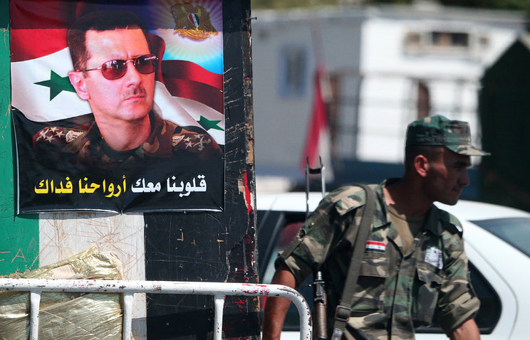 Syrian soldier near poster of Bashar al-Assad
