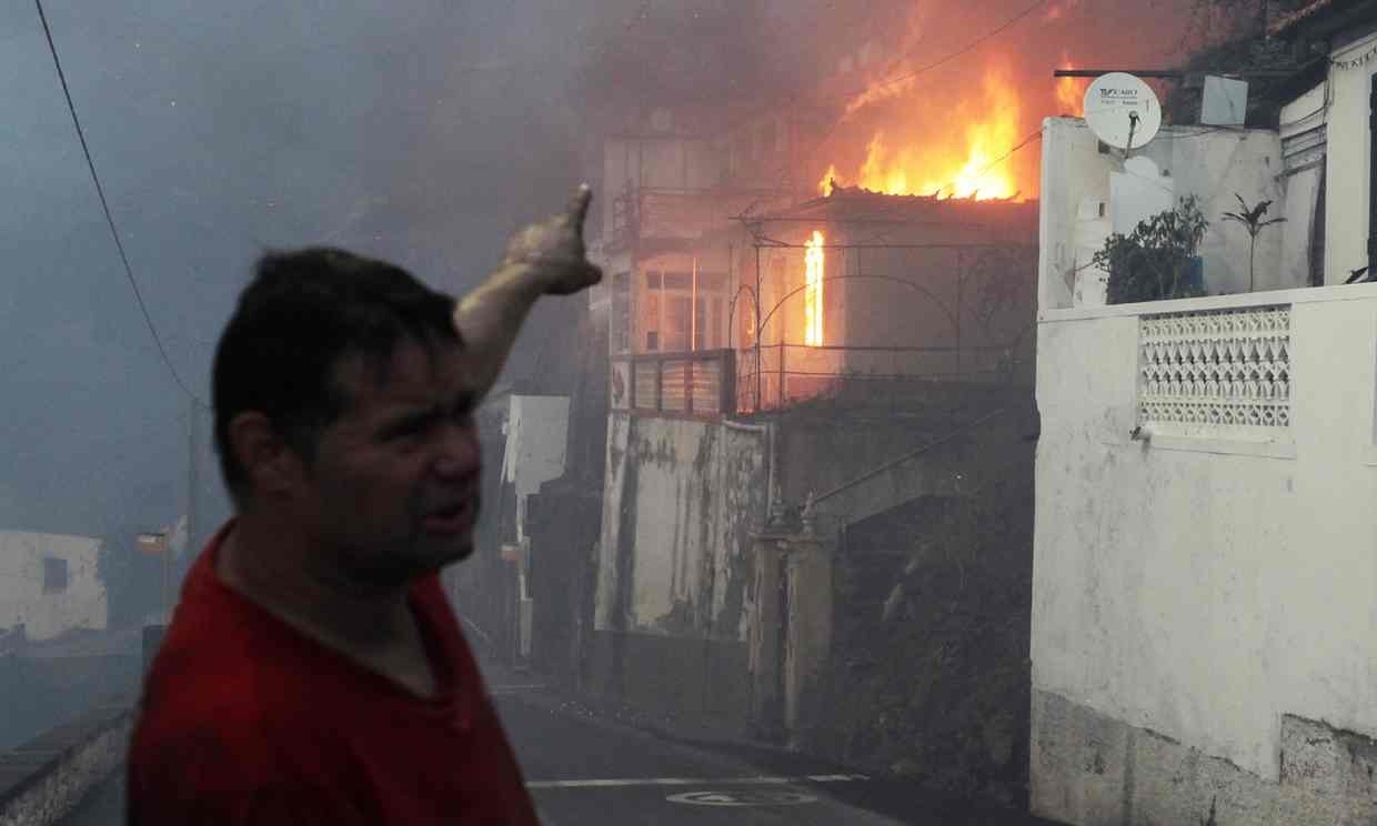 A man gestures at a burning house as a wildfire spreads at Bom Sucesso in Funchal. 