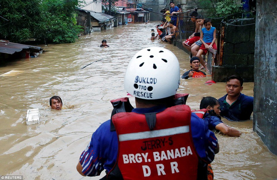 Rescuers (pictured) are seen rowing through the flooded streets trying to evacuate residents who can be seen clinging to debris that has become lodged in the deep currents 