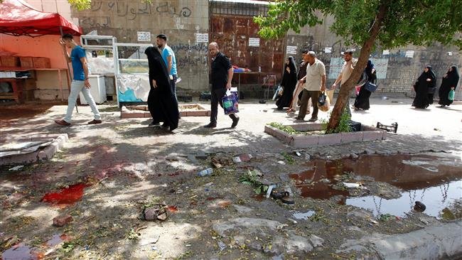 Click to enlarge Iraqis walk at the site of a bombing near a checkpoint in the Kadhimiyah area