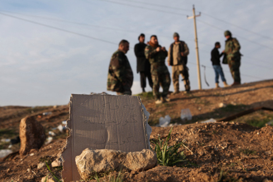 Kurdish Peshmerga forces inspect a site marked in Kurdish with a sign reading ‘Kurdish mass grave’ 