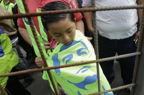 boy wears a banner with a stenciled image of Ecuador’s President Rafael Correa