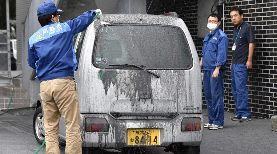 An officer of the city government cleans a car covered in volcanic ash which came from the eruptive crater of Mount Aso in Aso, Kumamoto prefecture, southwestern Japan