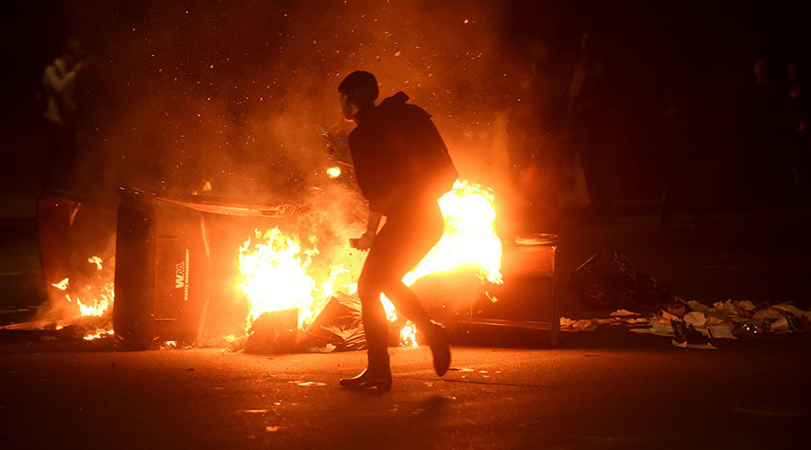 A woman passes burning garbage during a demonstration in Oakland, California, U.S. following the election of Donald Trump as President of the United States November 9, 2016