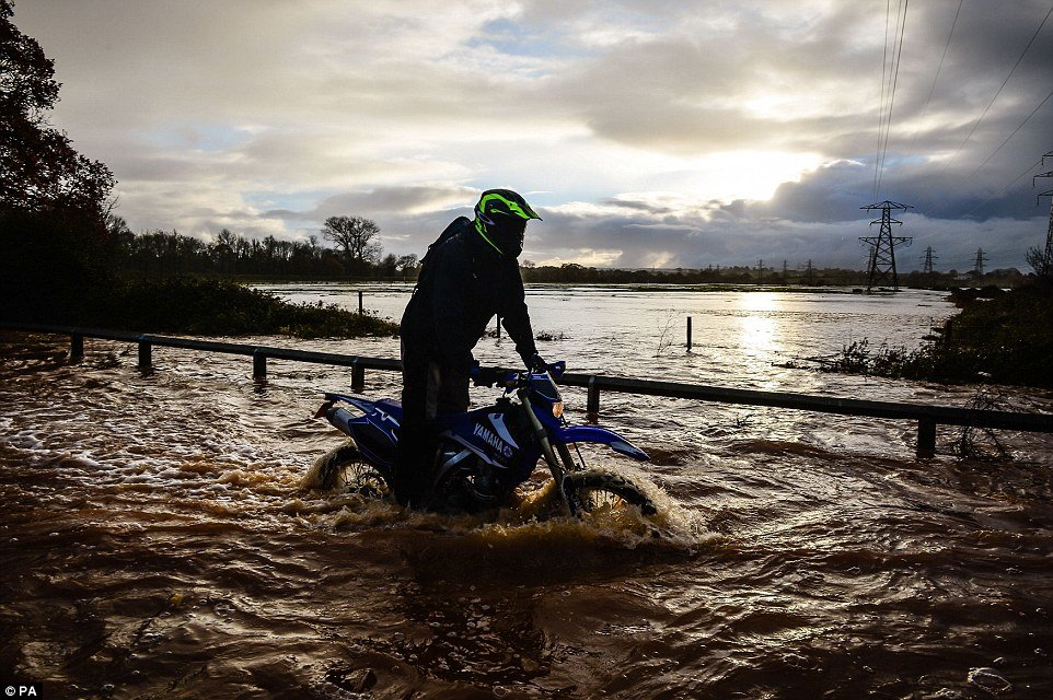 A biker ventures through deep flood water on Station Road, Broadclyst, Devon, where rivers have burst their banks and closed the main roads south of the village