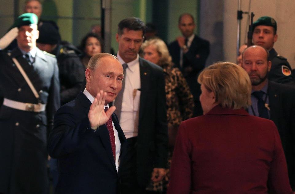 Vladimir Putin waves as he arrives with Angela Merkel 