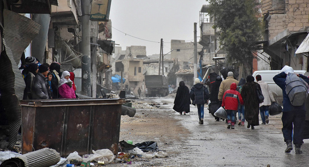 Syrian residents fleeing eastern part of Aleppo walk through a street in Masaken Hanano, a former rebel-held disctrict which was retaken by the govt forces last week