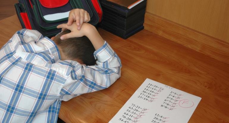 young boy hangs his head in shame after getting an F on his math test