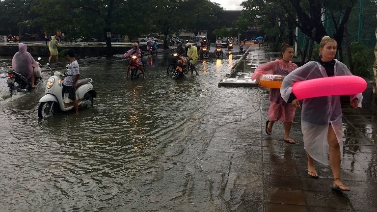 Tourists wear flotation devices and moped riders pause before crossing a flooded roadway on Ko Samui, Thailand Thursday, Jan. 5, 2017.