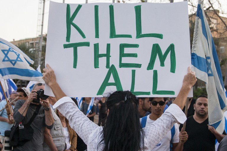 A woman holds up a sign with ‘Too many terrorists in prison’ written on one side and ‘Kill them all’