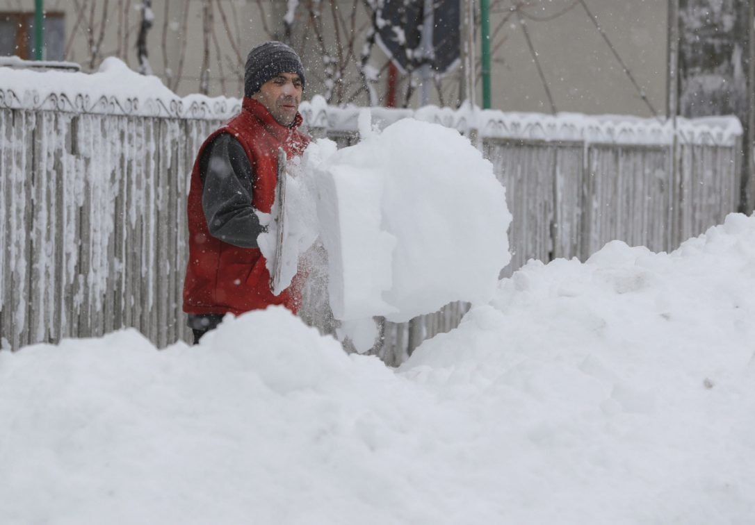 Click to enlarge A man shovels snow outside his home in Pietrosani, Romania. The blizzard is expected to ease off late Friday.