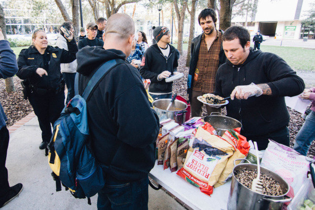 A volunteer serves food as police linger nearby.