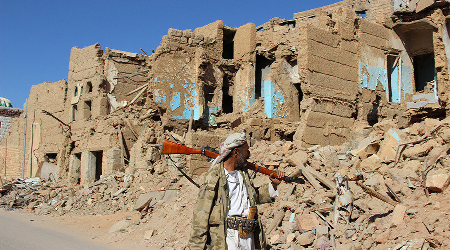 Houthi armed man walks past destroyed houses