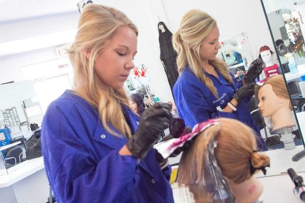 A cosmetologist in training colors hair on a mannequin at Victoria Beauty College
