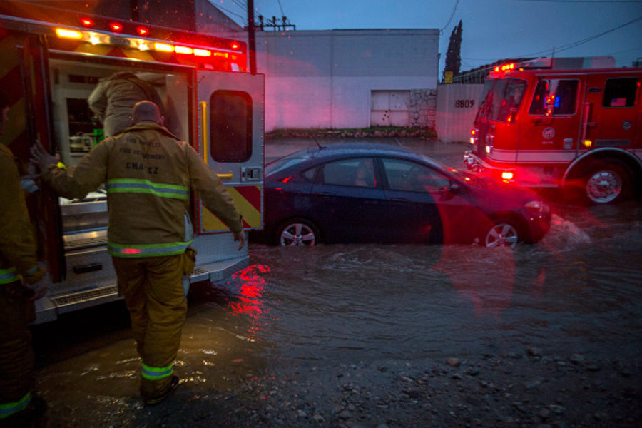 Firefighters prepare to transport a patient by ambulance at the scene of a car stuck in flooding as a powerful storm moves across Southern California on February 17, 2017 in Sun Valley, California.