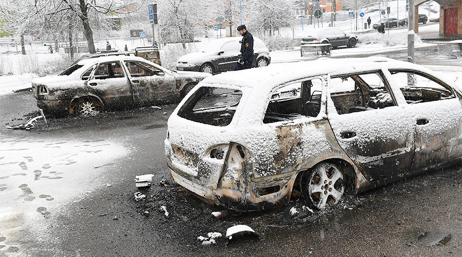 policeman investigates a burnt car in the Rinkeby suburb outside Stockholm, Sweden
