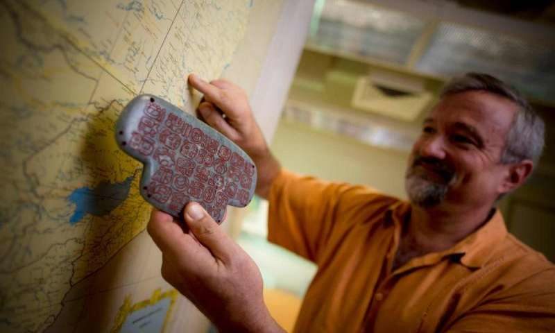 Click to enlarge UC San Diego archaeologist Geoffrey Braswell holds a replica of the Maya jade pendant
