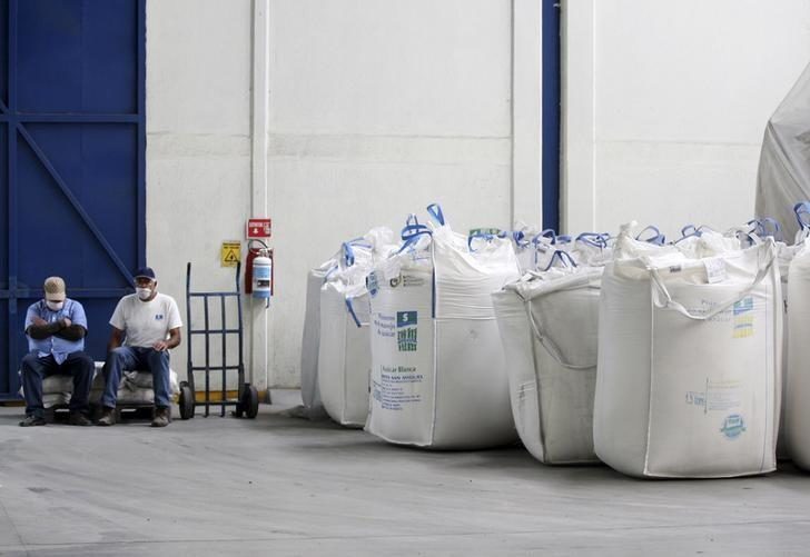 Workers sit next to bags containing sugar at the San Francisco