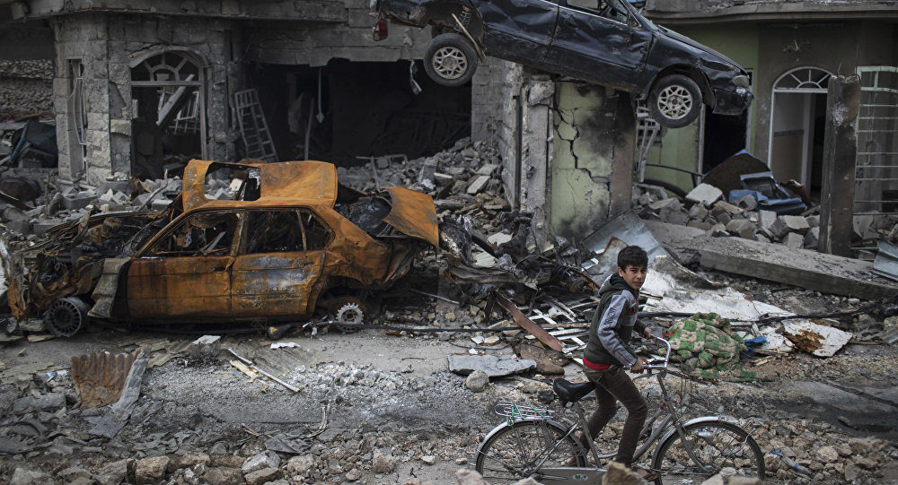 A boy rides his bike past destroyed cars and houses in a neighborhood recently liberated by Iraqi security forces, on the western side of Mosul, Iraq, Sunday, March 19, 2017