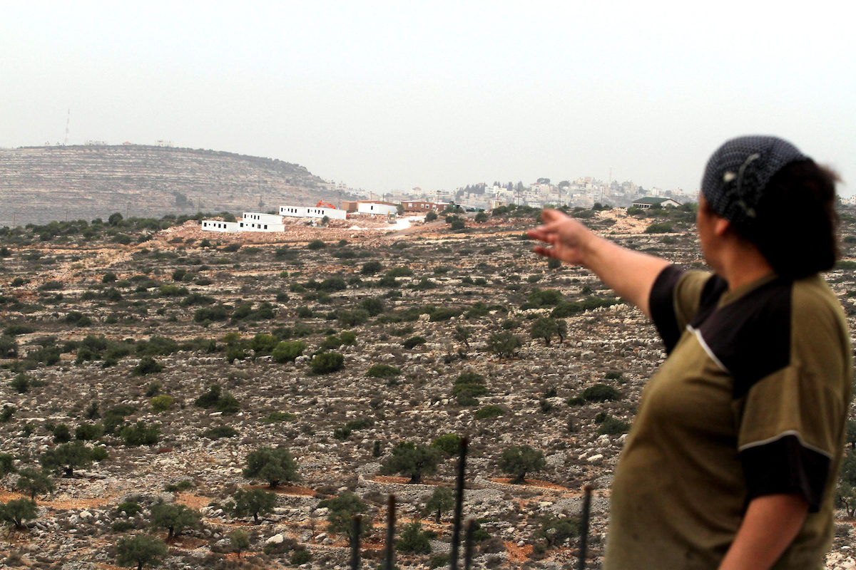 Palestinian woman looks at bungalows in the distance built by Israeli settlers