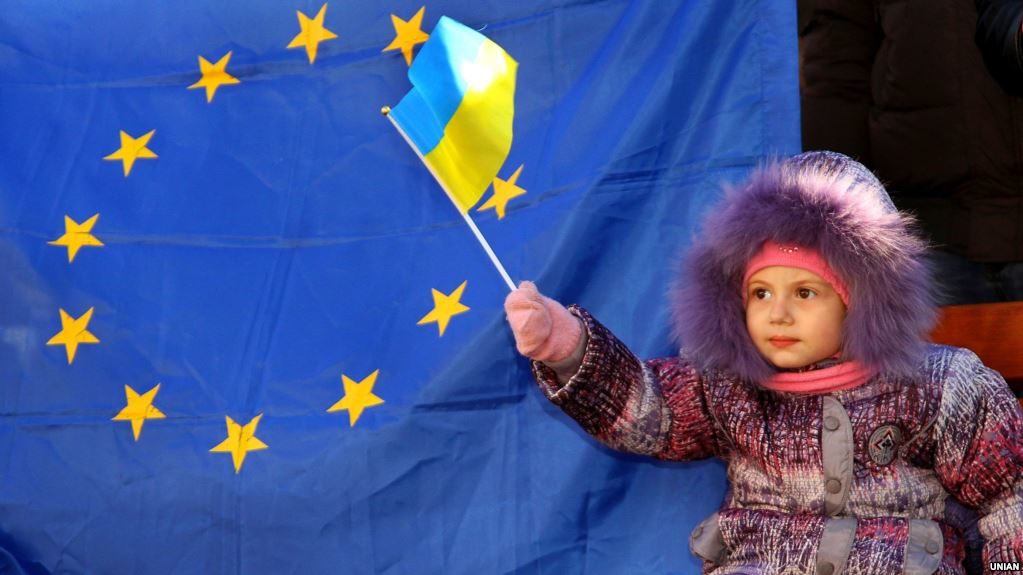 Child holding Ukraine flag near EU flag