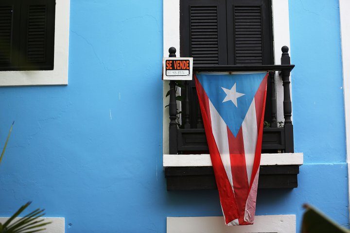 Click to enlarge or sale sign is seen hanging from a balcony next to a Puerto Rican flag