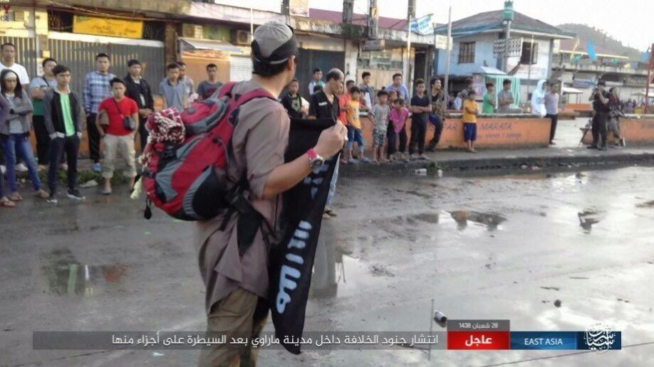 A man carries the ISIS flag of conquest in front of stoic locals