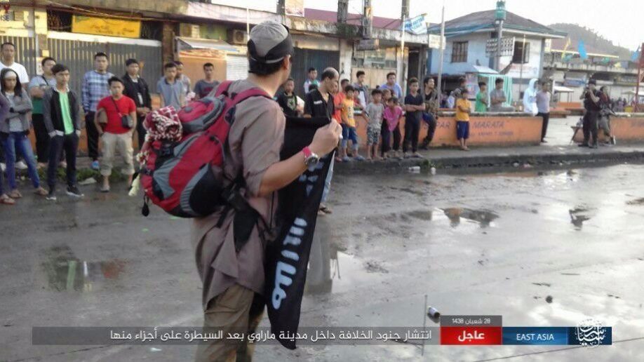 Click to enlarge A man carries the ISIS flag of conquest in front of stoic locals
