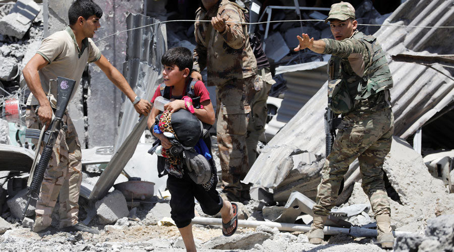 A man carries his child as he runs to a safer place near an Iraqi soldier standing guard in Mosul