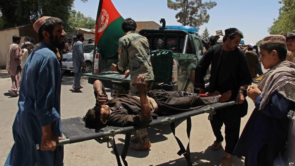 Afghan men carry a victim of a powerful car bomb in Lashkar Gah