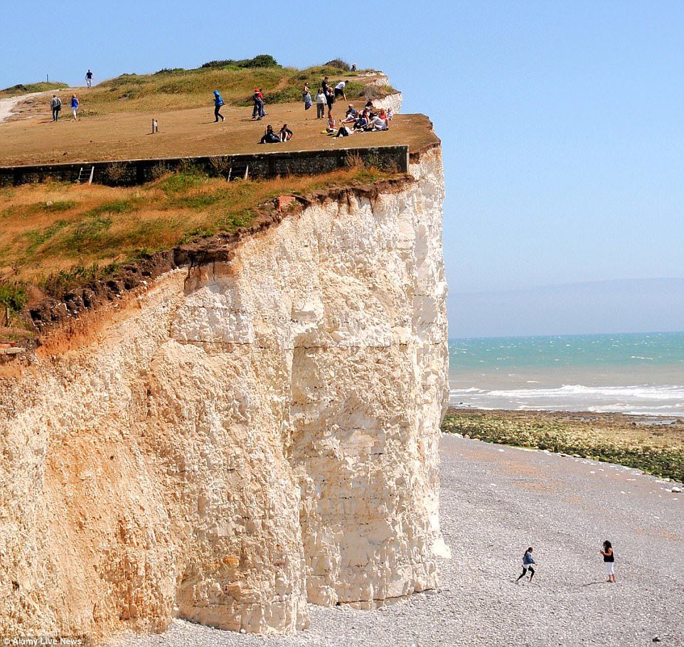 Click to enlarge Dozens of people were seen happily having picnics and exploring the cliff's edge while two other explorers were seen walking on the beach underneath