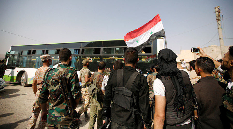 Syrian Army soldiers wave the Syrian national flag as civilians ride buses